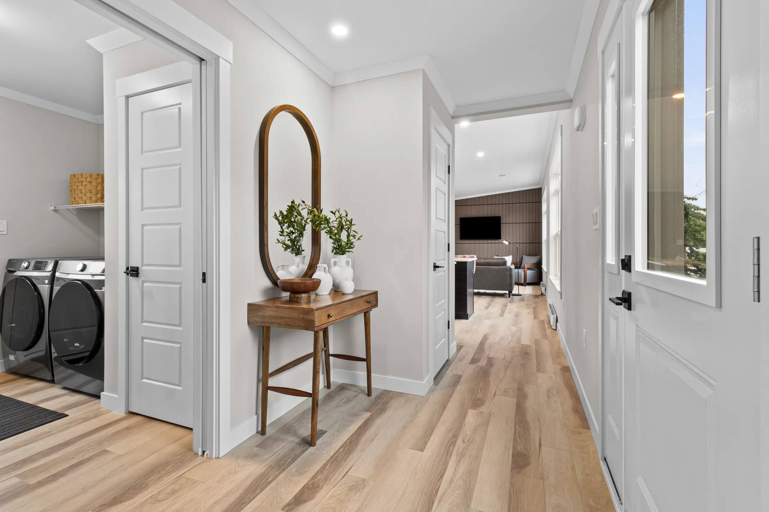 Welcoming entry hallway with light wood flooring, a decorative console table, laundry room access, and views toward the open-concept living area. 