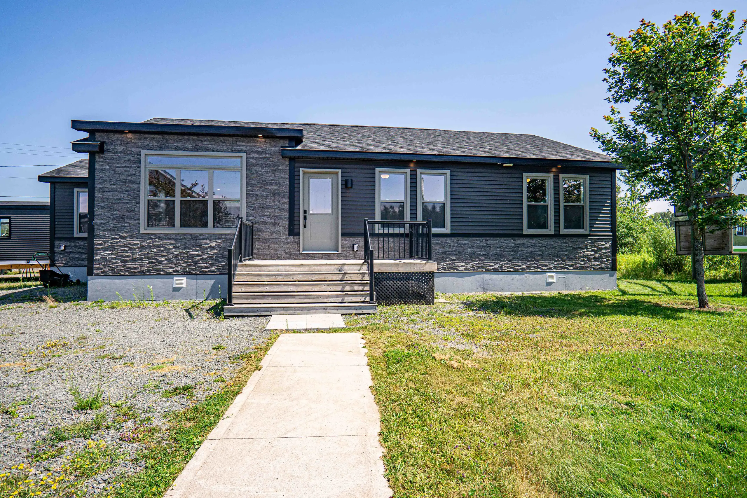Modern bungalow with dark siding, stone-accented exterior, large front window, and a welcoming entry deck with stairs. 