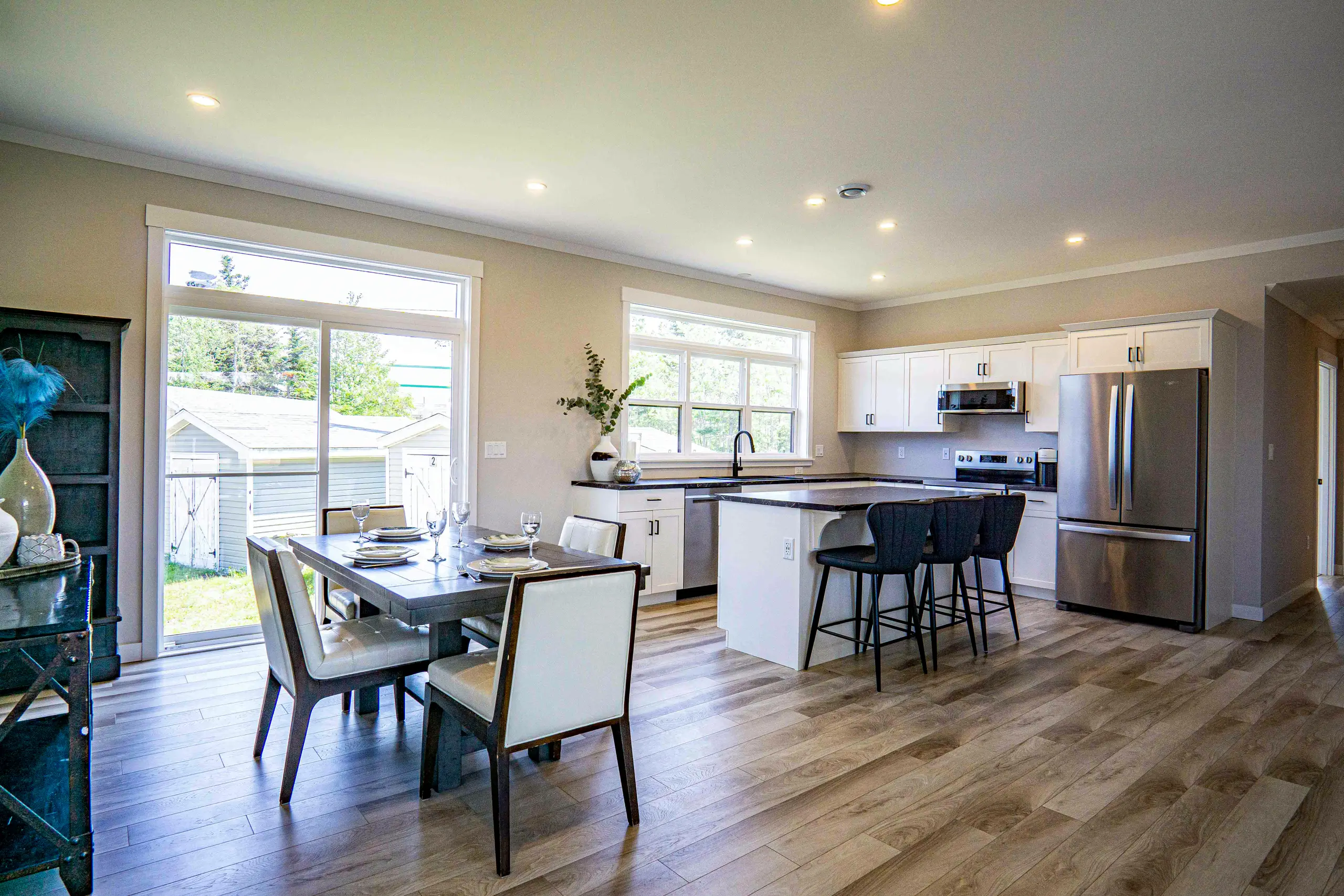 Open-concept kitchen and dining space with white cabinetry, stainless steel appliances, large island seating, and patio door access. 