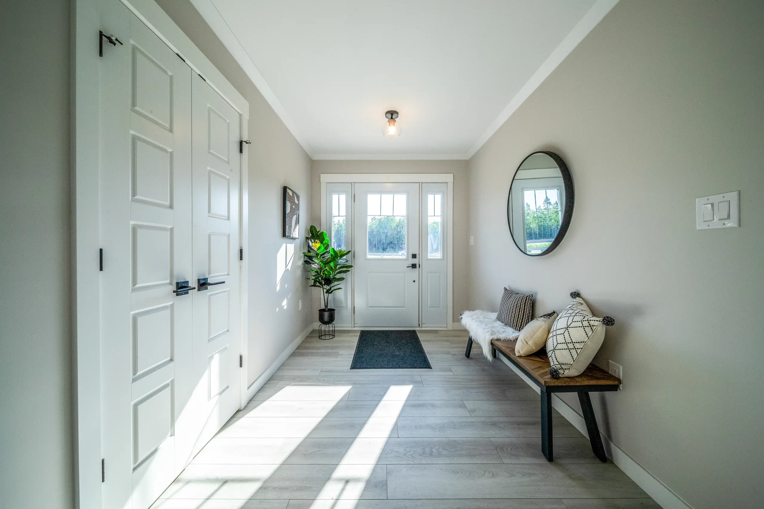 Bright front entryway with a white front door, double closet, bench seating, round mirror, and light wood-look flooring. 