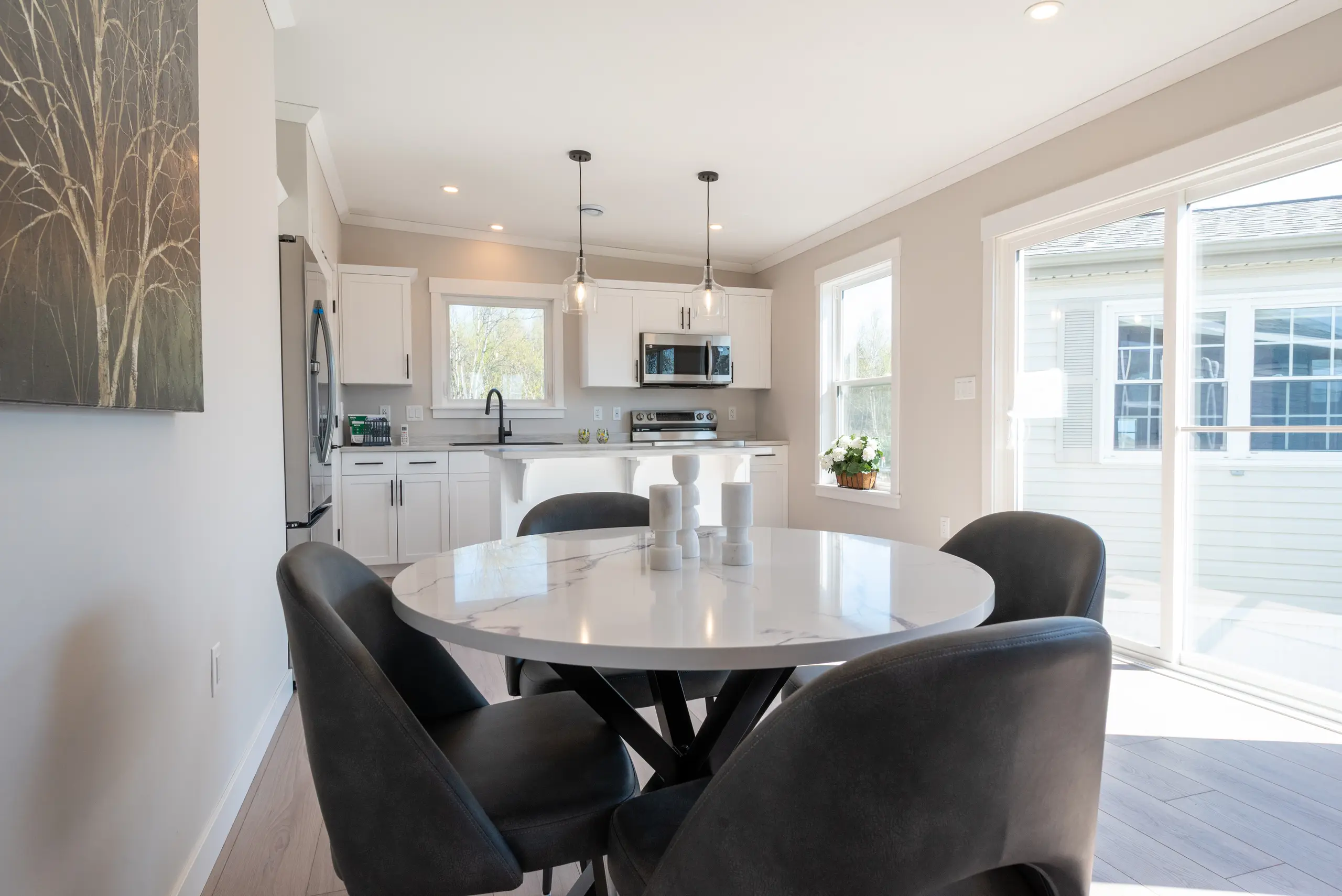 Open dining area with a round table and upholstered chairs, flowing into a modern white kitchen with stainless steel appliances. 