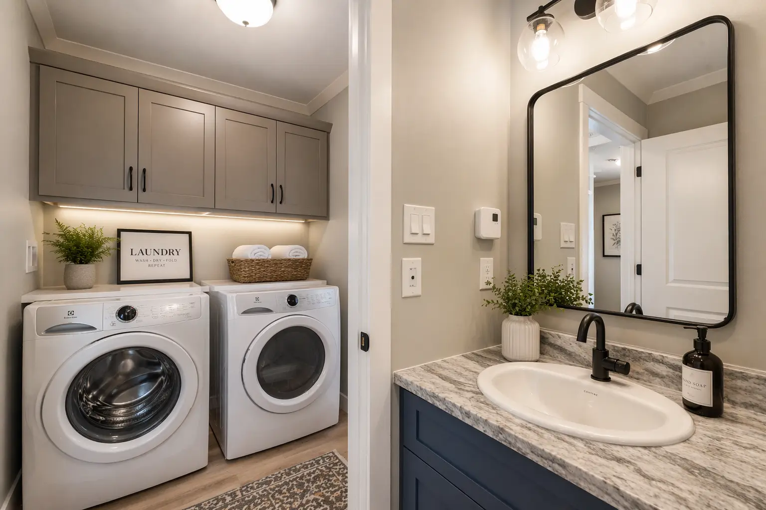 Compact laundry and bathroom space featuring front-load appliances, overhead cabinetry, a navy blue vanity, and modern black fixtures. 